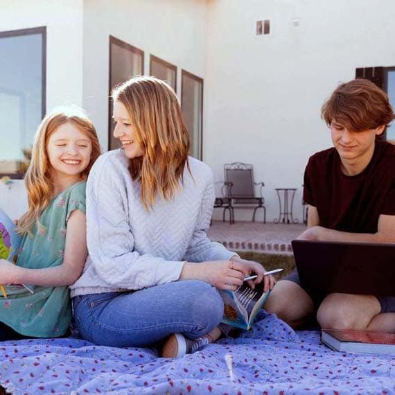 Family of three sitting on a blanket outside while learning - Connections Academy